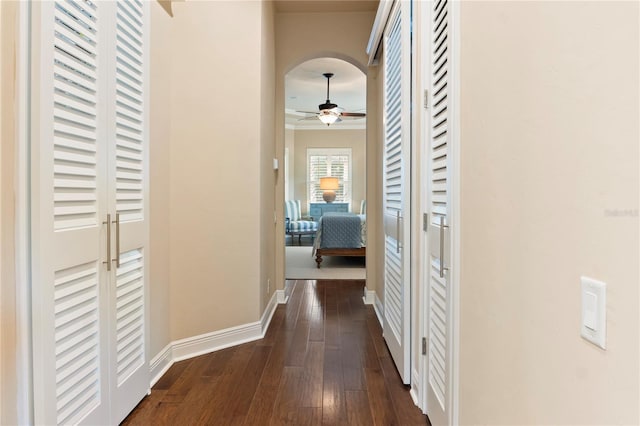 corridor featuring dark wood-type flooring, baseboards, and arched walkways