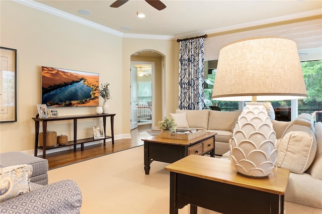 living area featuring a ceiling fan, arched walkways, crown molding, wood finished floors, and baseboards