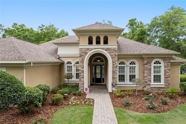 mediterranean / spanish-style home with stucco siding, stone siding, and roof with shingles