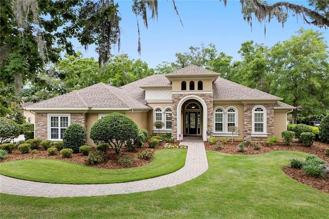 mediterranean / spanish home featuring stone siding, stucco siding, and a front lawn