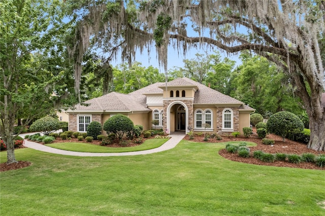 mediterranean / spanish home featuring stone siding, stucco siding, and a front yard