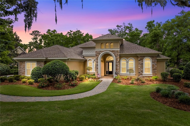 mediterranean / spanish-style home with stone siding, stucco siding, and a lawn