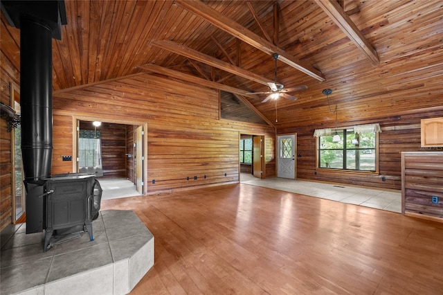 unfurnished living room featuring wooden walls, ceiling fan, wood ceiling, and a wood stove