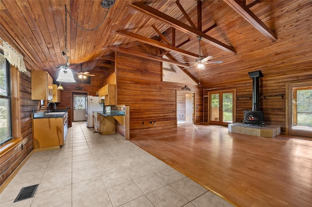 unfurnished living room with wood ceiling, ceiling fan, visible vents, a wood stove, and wooden walls