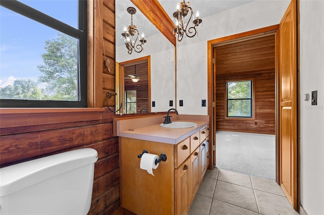 half bath featuring tile patterned flooring, vanity, toilet, wooden walls, and a notable chandelier