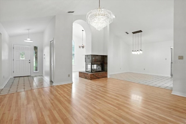 7800 SW 24th Ave, Gainesville, FL 32607 - unfurnished living room with a chandelier, light wood finished floors, vaulted ceiling, arched walkways, and a fireplace
