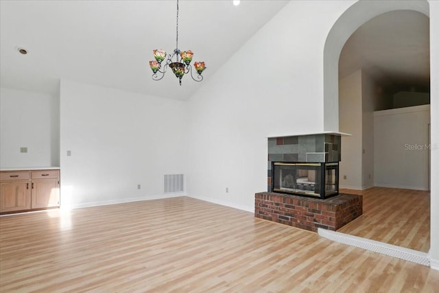 7800 SW 24th Ave, Gainesville, FL 32607 - unfurnished living room featuring high vaulted ceiling, light wood finished floors, arched walkways, a brick fireplace, and a chandelier