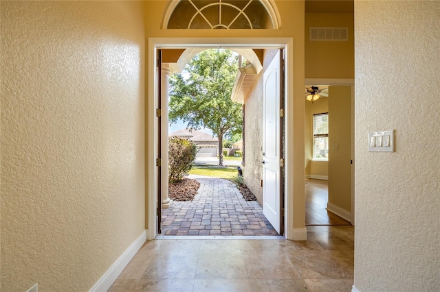entryway featuring visible vents, a textured wall, ceiling fan, and baseboards