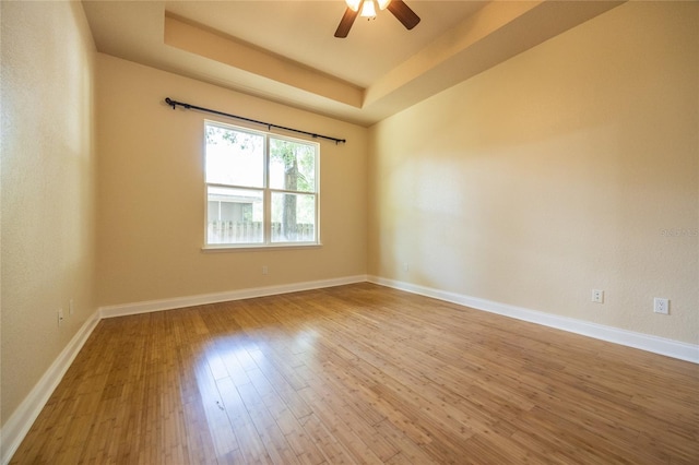 empty room with baseboards, a ceiling fan, a tray ceiling, and wood finished floors