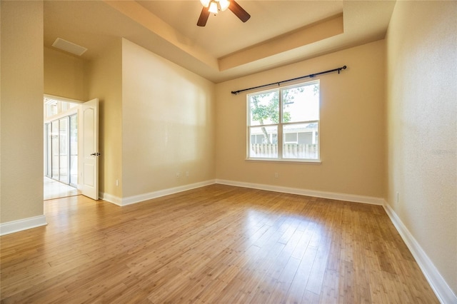 unfurnished room with ceiling fan, visible vents, wood finished floors, a raised ceiling, and baseboards