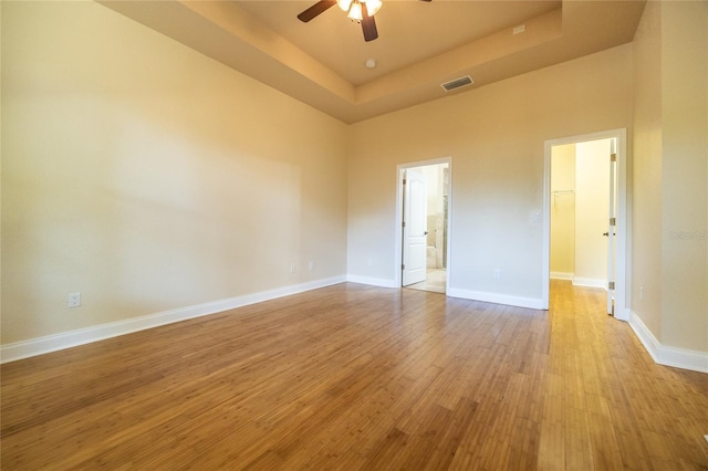 empty room with ceiling fan, light wood-style floors, baseboards, a tray ceiling, and visible vents