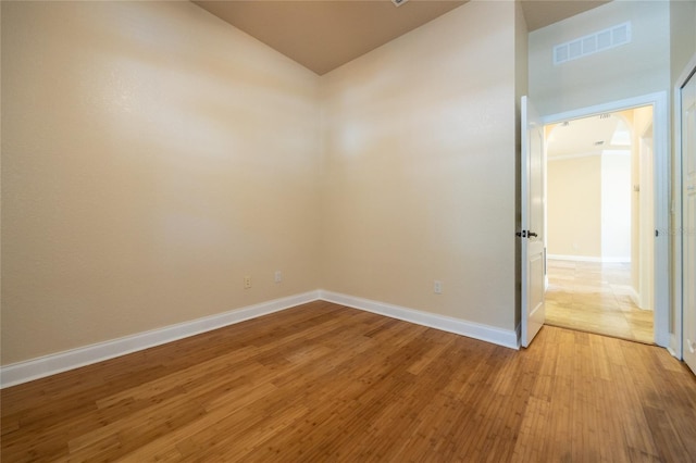 spare room featuring light wood-style floors, baseboards, vaulted ceiling, and visible vents