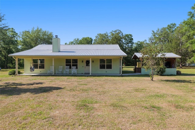 back of house with covered porch, a standing seam roof, metal roof, a chimney, and a lawn