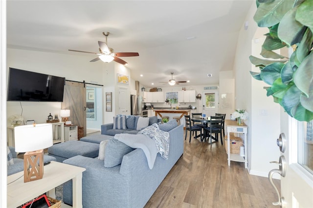 living area with ceiling fan, vaulted ceiling, a barn door, wood finished floors, and baseboards