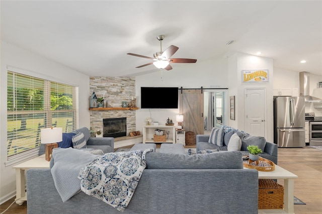 living area with lofted ceiling, light wood-style floors, a stone fireplace, ceiling fan, and a barn door