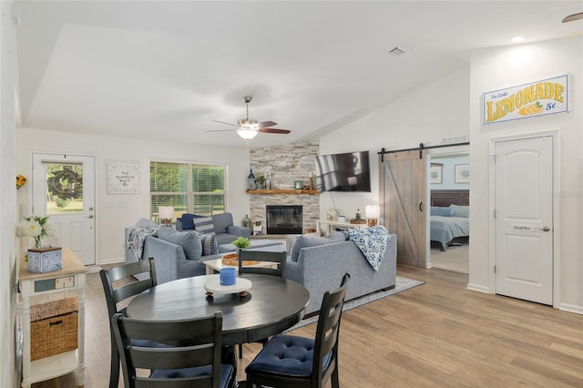 dining area featuring lofted ceiling, a stone fireplace, light wood-style floors, ceiling fan, and a barn door