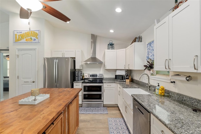 kitchen featuring wall chimney range hood, appliances with stainless steel finishes, a sink, butcher block countertops, and light wood-style flooring