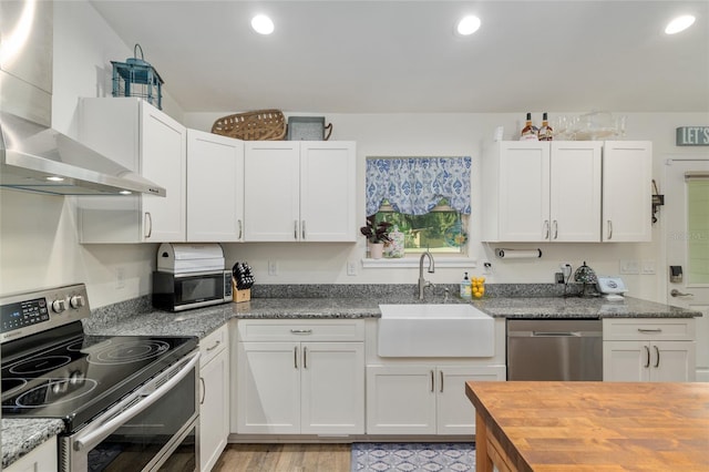 kitchen with appliances with stainless steel finishes, a sink, wooden counters, wall chimney exhaust hood, and white cabinetry