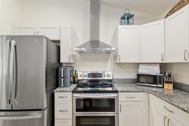 kitchen with light stone counters, wall chimney exhaust hood, appliances with stainless steel finishes, and white cabinets