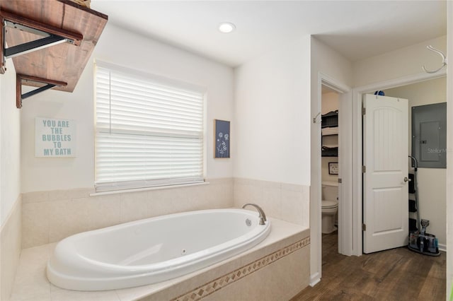 bathroom featuring toilet, a wealth of natural light, wood finished floors, and a bath