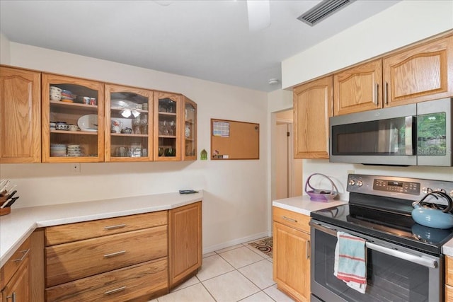 kitchen with visible vents, glass insert cabinets, light countertops, light tile patterned floors, and stainless steel appliances