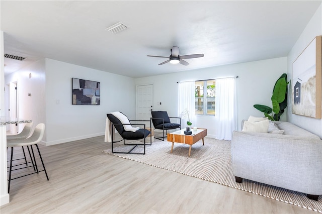 living area with visible vents, a ceiling fan, light wood finished floors, and baseboards