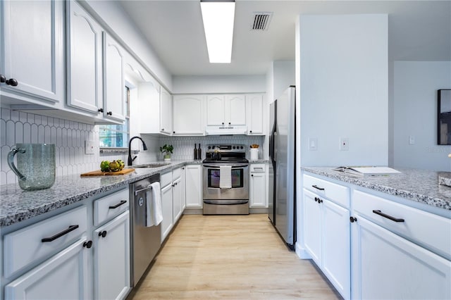 kitchen with light stone countertops, appliances with stainless steel finishes, a sink, and light wood finished floors