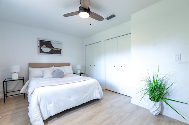 bedroom with multiple closets, a ceiling fan, light wood-type flooring, and visible vents