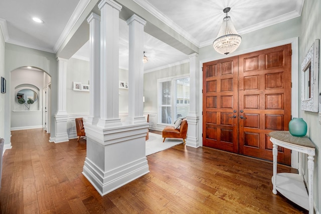 foyer entrance with ornate columns, arched walkways, dark wood-type flooring, and ornamental molding