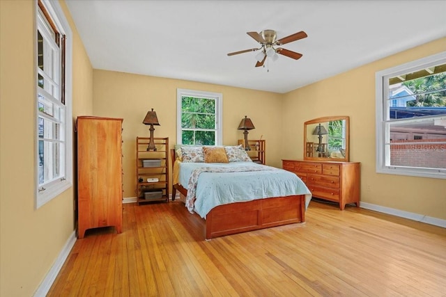 bedroom featuring baseboards, a ceiling fan, light wood-style flooring, and multiple windows