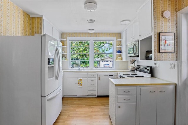 kitchen with open shelves, white appliances, light countertops, a sink, and light wood-style flooring