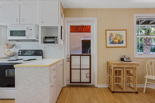 kitchen featuring white microwave, light countertops, electric range oven, white cabinetry, and light wood finished floors