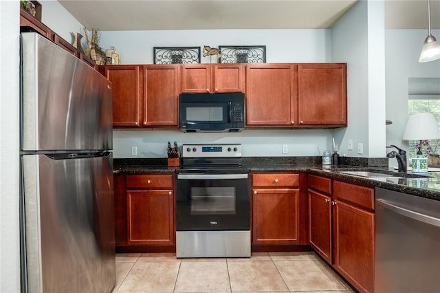 kitchen featuring appliances with stainless steel finishes, hanging light fixtures, a sink, dark stone counters, and light tile patterned floors