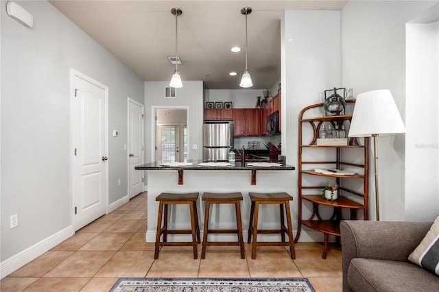 kitchen with a kitchen bar, black microwave, dark countertops, freestanding refrigerator, and light tile patterned flooring