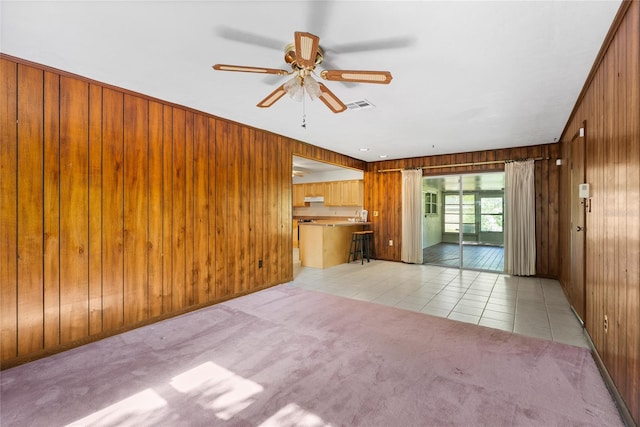 5620 NW 25th St, Gainesville, FL 32653 - unfurnished living room featuring wood walls, light colored carpet, visible vents, a ceiling fan, and light tile patterned floors
