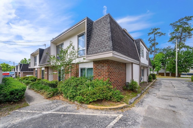 view of side of home with mansard roof, brick siding, and a shingled roof