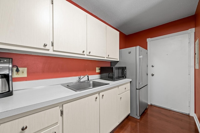 kitchen with a sink, a textured ceiling, dark wood-type flooring, black microwave, and light countertops