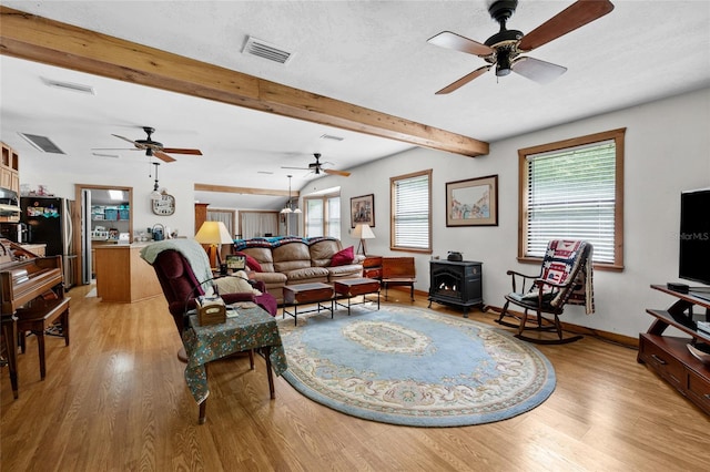 living room with visible vents, a wood stove, baseboards, a ceiling fan, and light wood finished floors