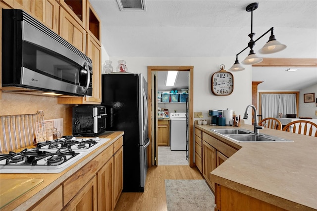 kitchen with appliances with stainless steel finishes, a sink, light countertops, light wood-style flooring, and washer / clothes dryer