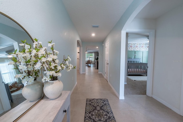 corridor with visible vents, light tile patterned flooring, baseboards, a textured ceiling, and arched walkways