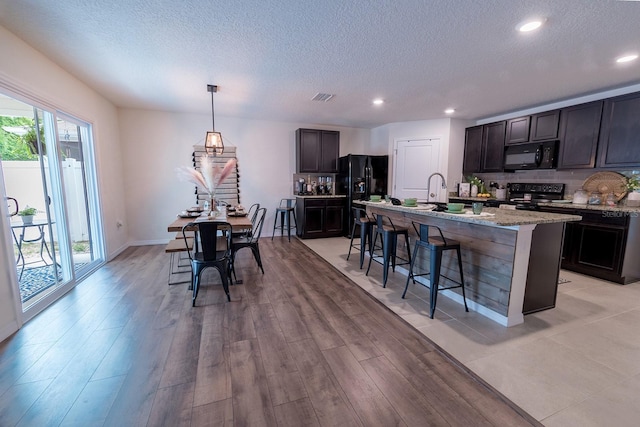 kitchen featuring a breakfast bar area, black appliances, a textured ceiling, and visible vents