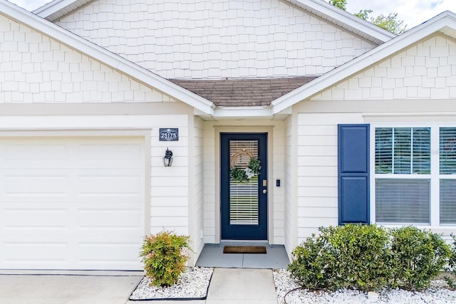 view of exterior entry with roof with shingles and an attached garage