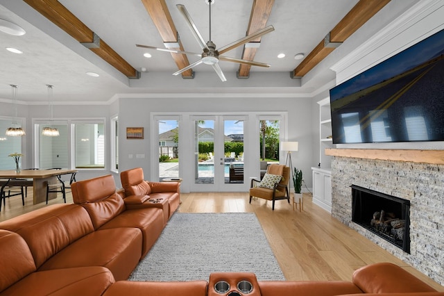 living room with light wood-type flooring, ceiling fan, beamed ceiling, a stone fireplace, and french doors