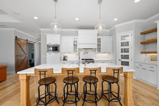 kitchen with appliances with stainless steel finishes, a barn door, backsplash, light wood-type flooring, and ornamental molding
