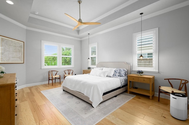 bedroom featuring a tray ceiling, light wood-style flooring, baseboards, crown molding, and ceiling fan