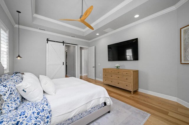 bedroom featuring a raised ceiling, a barn door, light wood-type flooring, baseboards, and crown molding