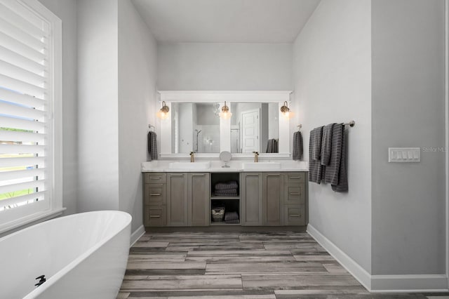 bathroom featuring double vanity, wood finished floors, a soaking tub, a shower stall, and baseboards