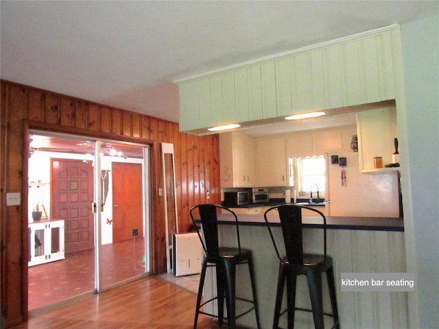 kitchen featuring a peninsula, wooden walls, light wood-style flooring, a kitchen bar, and dark countertops