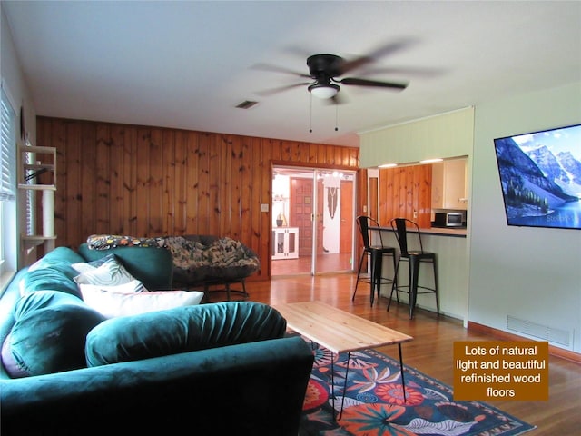 living area with visible vents, wood finished floors, a ceiling fan, and wooden walls