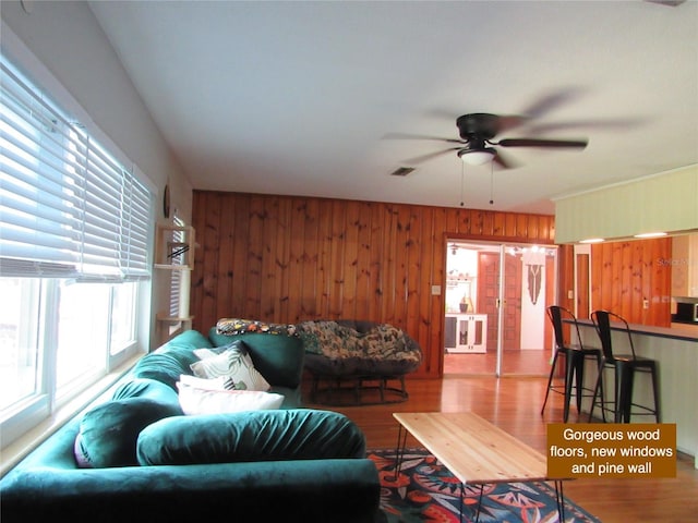 living room with wooden walls, a ceiling fan, visible vents, and wood finished floors